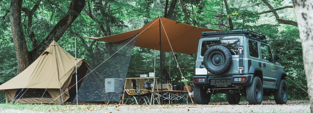 森の中で設営されたテントとタープ、四駆車のキャンプサイトの様子。