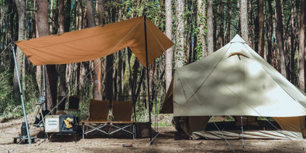 キャンプ場で木々の前でテントを2基設営している様子